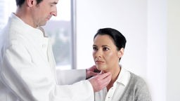 Das Bild zeigt einen Arzt, der die Schilddrüse bei einer Patientin abtastet.