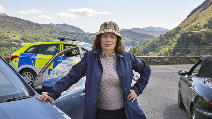Detektive Inspector Morgan (Teresa Harder) steht vor einem Polizeiwagen und nimmt die Suche nach der Vermissten wieder auf.