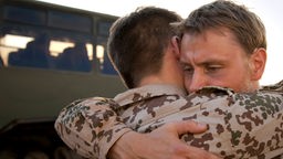 Zwei Soldaten in Einsatzkleidung umarmen sich vor einem Bus.