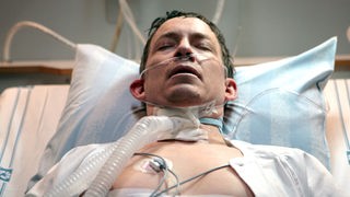 Ein Mann liegt, angeschlossen an lebenserhaltende Geräte, in einem Krankenhausbett