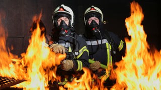 Feuerwehrleute mit Atemmasken vor lodernden Flammen