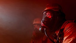 Zwei Feuerwehrmänner mit Atemschutzmasken in einem rauchverhangenen Raum