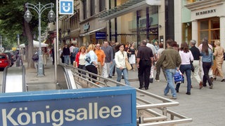 Blick auf die Kö, im Vordergrund ein U-Bahn-Schild mit "Königsalle" darauf.