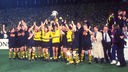 Gelb-Schwarz gekleidetet Fußballspieler halten gemeinsam einen Pokal hoch und freuen sich