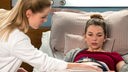 Eine Frau liegt mit Wehen in einem Krankenbett, neben ihr eine Ärztin