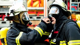 Zwei Feuerwehrmänner schließen sich während einer Übung vor einem Löschfahrzeug die Atemschutzgeräte an