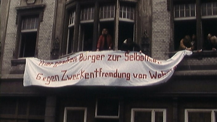 Hausbesetzer halten ein Banner aus den Fenstern mit der Aufschrift "Hier greifen Bürger zur Selbst
