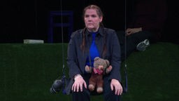 Melanie Hach bei der Inszenierung "Kinderhäuser" im Theater Münster. Melanie Hach sitzt mit einem Kuscheltier auf einer Schaukel.