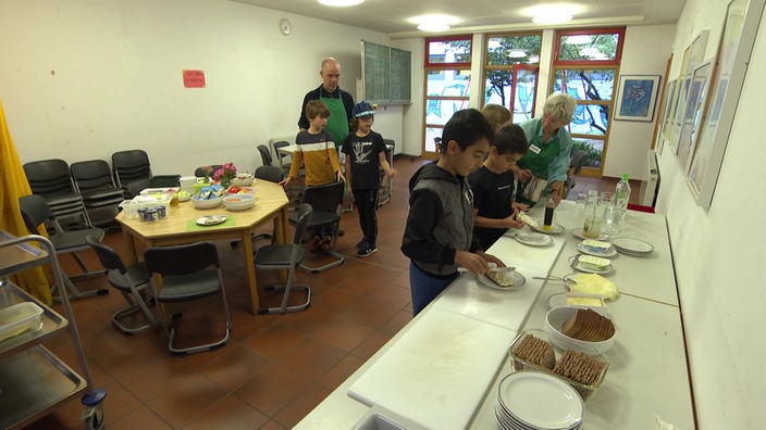 Kinder und Lehrer:innen schauen sich das Frühstücksangebot der Primusschule Münster genau an.