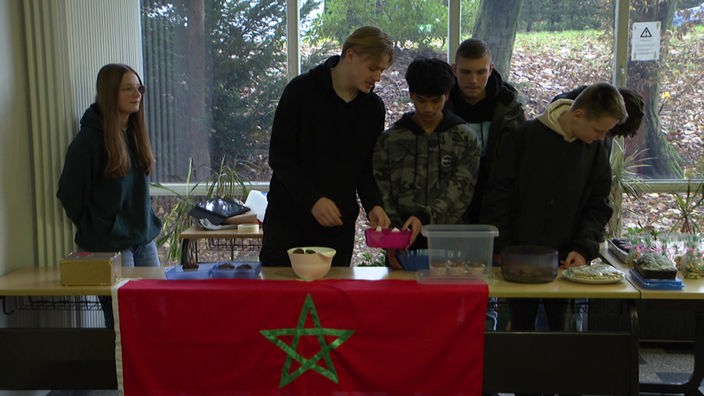 Schüler:innen bereiten einen Spenden-Kuchenverkauf vor. An ihrem Tisch hängt die Flagge Marokkos.