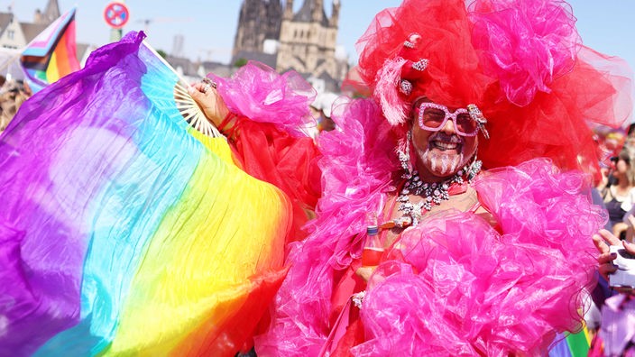 Eine Person mit Regenbogenfahne nimmt an der Paprade des Christopher Street Day in Köln teil.