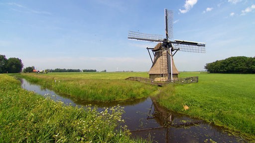 Windmühle auf grüner Wiese neben einem Wasserlauf