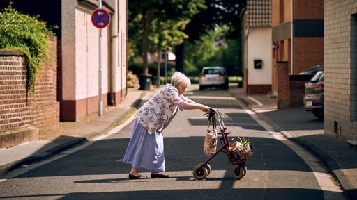 Eine alte Frau schiebt einen Rollator über die Straße 