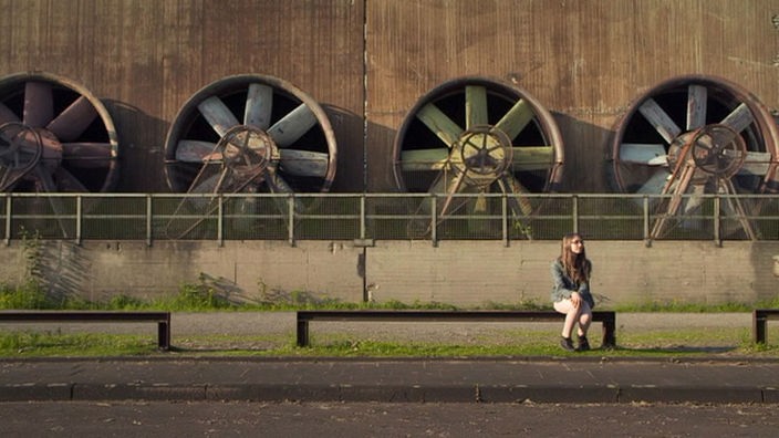 Mädchen sitzt auf einer Mauer vor vier großen Turbinen