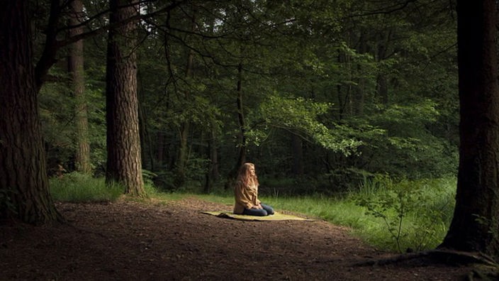 Ein Mädchen kniet auf einer Decke im Wald