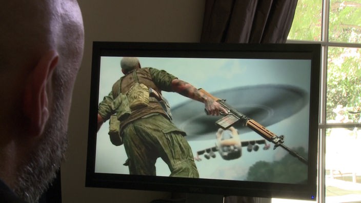 Ein Mann sitzt vor einem Computerbildschirm, auf dem ein Soldat mit Waffe geht