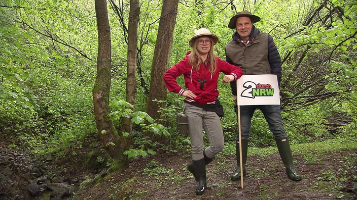 Esther und André im Wald mit einem Schild mit der Aufschrift "2 durch NRW"