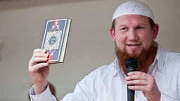 Pierre Vogel als Redner mit Mikrofon und einem Koran in der Hand bei einer salafistischen Verkündigungsveranstaltung