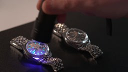 Das Bild zeigt zwei sich ähnelnde Uhren. Sie werden mit einer Taschenlampe untersucht.  