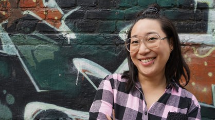 Shia Su lächelnd vor einem Graffiti-Hintergrund