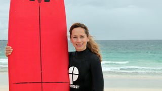 Tamina Kallert mit einem roten Surfbrett amStrand