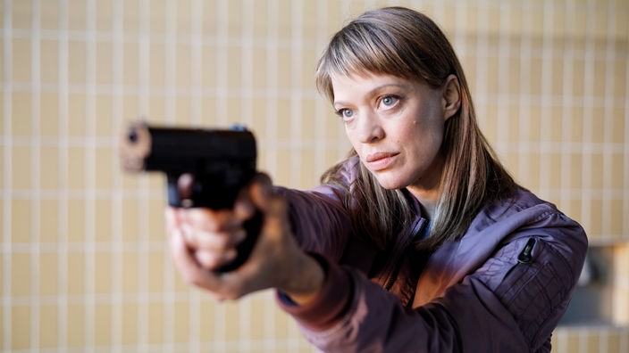 Ellen Berlinger, gespielt von Heike Makatsch, hält eine Waffe nach oben.