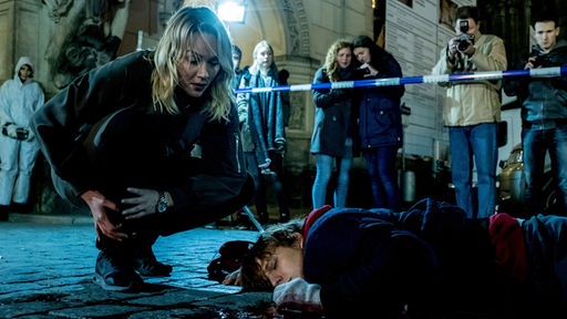 Szene aus dem Tatort Dresden "Level X": Komissarin beugt sich über Leiche, die auf Straße liegt