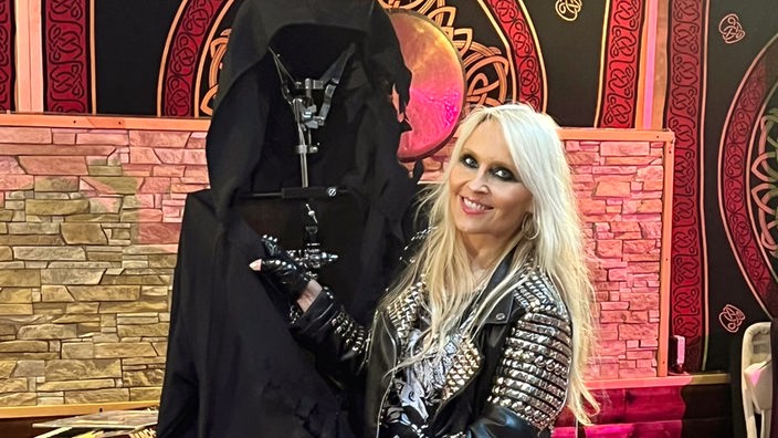 Metal-Sängerin Doro Pesch steht neben einer auf einem Metalgestell aufgebauten schwarzen Kutte.