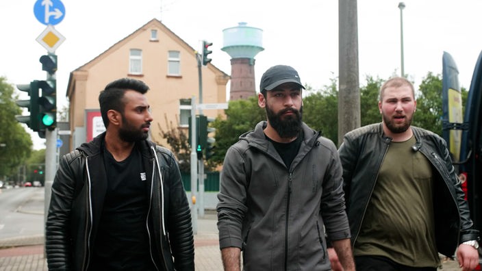 drei junge Männer gehen auf der Straße auf die Kamera zu