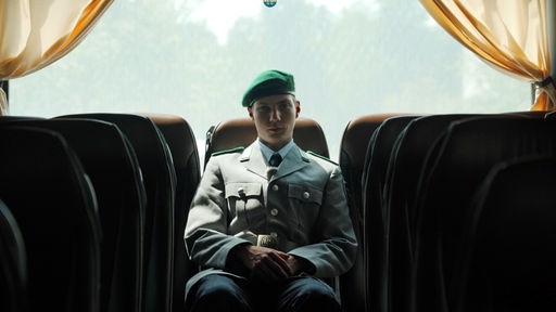 Ein junger Soldat in Ausgeh-Uniform sitzt allein auf der Rückbank eines Busses