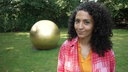 Siham El-Maimouni steht vor einer goldenen Kugel. Die Skulptur steht im Skulpturenpark Köln.