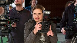Eine Frau mit Fotokamera in der Hand blickt gebannt auf eine Szene vor sich  
