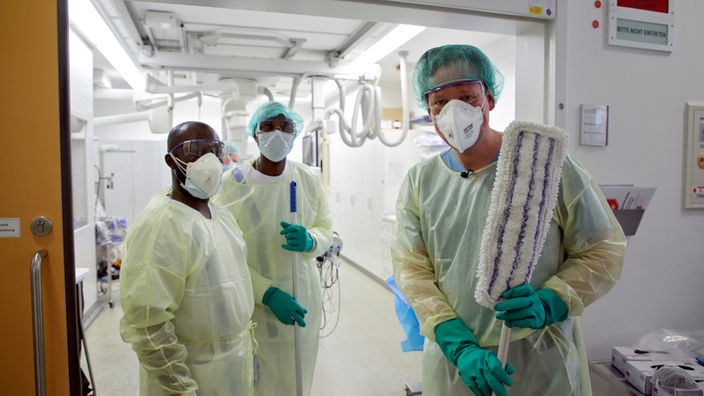 Eckart von Hirschhausen und zwei Mitarbeiter der Uniklinik Bonn in medizinischer Schutzkleidung 