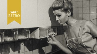 Eine Frau spricht in der Küche über ein Gerät mit ihrem Mann im Wohnzimmer