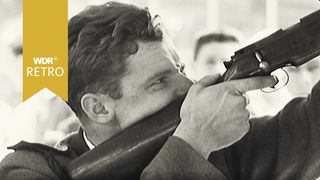 Schwarz-Weiß Aufnahme eines Mannes der ein Gewehr in der Hand hält.