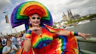 Ein Teilnehmer in einem Regenbogen-Kostüm steht bei der Parade zum Christopher Street Day vor dem Kölner Dom.
