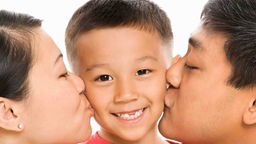 Kind bekommt einen Kuss von seinen Eltern