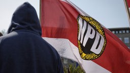 NPD-Fahne und ein Mensch mit Kapuze bei einer Demonstration