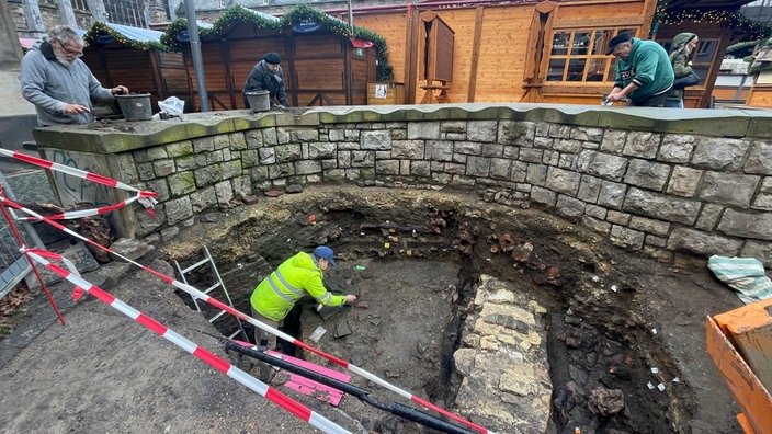 Ein Mann in Arbeitskleidung steht in einer Grube und gräbt archäologische Funde aus.