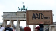 Menschen stehen vor dem Brandenburger Tor, ein Schild mit Aufschrift "#AfDnee" wird in die Höhe gehalten.