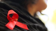 Eine Frau hat sich eine rote Aids-Schleife an die Jacke geheftet