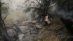 Mann geht an einem Haus vorbei, das bei einem Waldbrand in der algerischen Provinz Bouira niedergebrannt ist