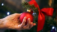 Hand einer Seniorin mit Weihnachtskugel