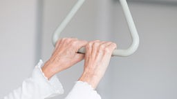 Hände einer älteren Frau umfassen den Aufrichttbügel am ihrem Krankenbett