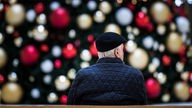 Ein alter Mann sitzt alleine vor einem Weihnachtsbaum