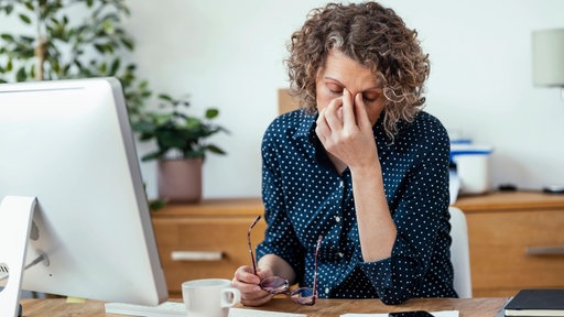 Eine erschöpfte arebeitende Person sitzt am Schreibtisch