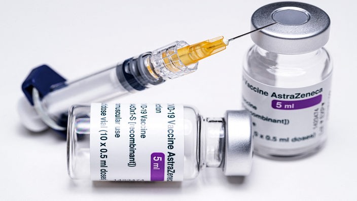 Eine Spritze lehnt an zwei Ampullen des Astrazeneca-Impfstoffs