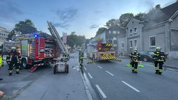 Einsatzfahrzeuge der Feuerwehr stehen auf der Straße vor dem brennenden Haus in Dortmund
