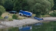 Ein Leichenwagen und ein Fahrzeug mit Boot des Technischen Hilfswerks (THW) stehen am Eiserbachsee