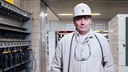 Der Steiger Andreas Schreiter steht im weißen Arbeitsanzug, mit Helm, Geleucht am Helm und Schutzbrille in der Lampenstube der Zeche Prosper Haniel